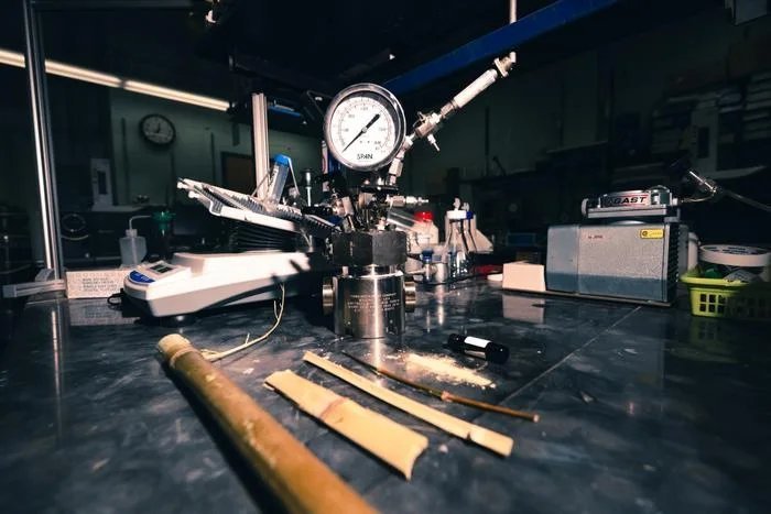 Banco de laboratorio con cañas de bambú, polvo de bambú, un frasco de biocrudo y un reactor metálico al fondo
